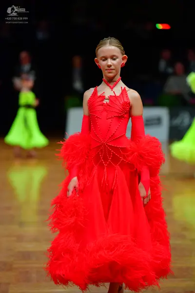 Dancesport competitor: Female dancer in foreground: red latin dress with feather trim, beaded web desig