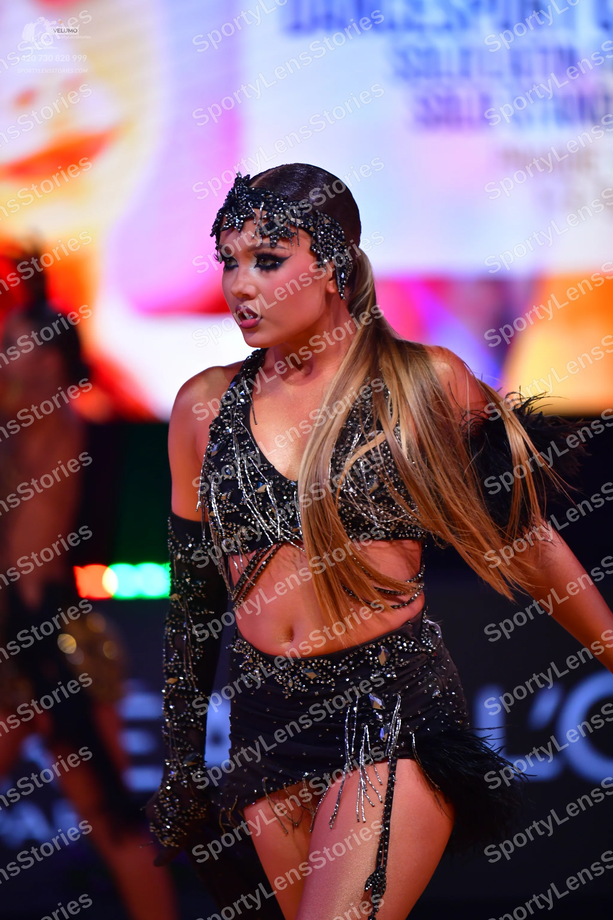 Dancesport competitor: Female dancer: black two-piece Latin dance costume with sequins and fringe, feat