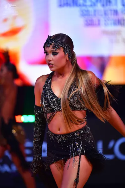 Dancesport competitor: Female dancer: black two-piece Latin dance costume with sequins and fringe, feat
