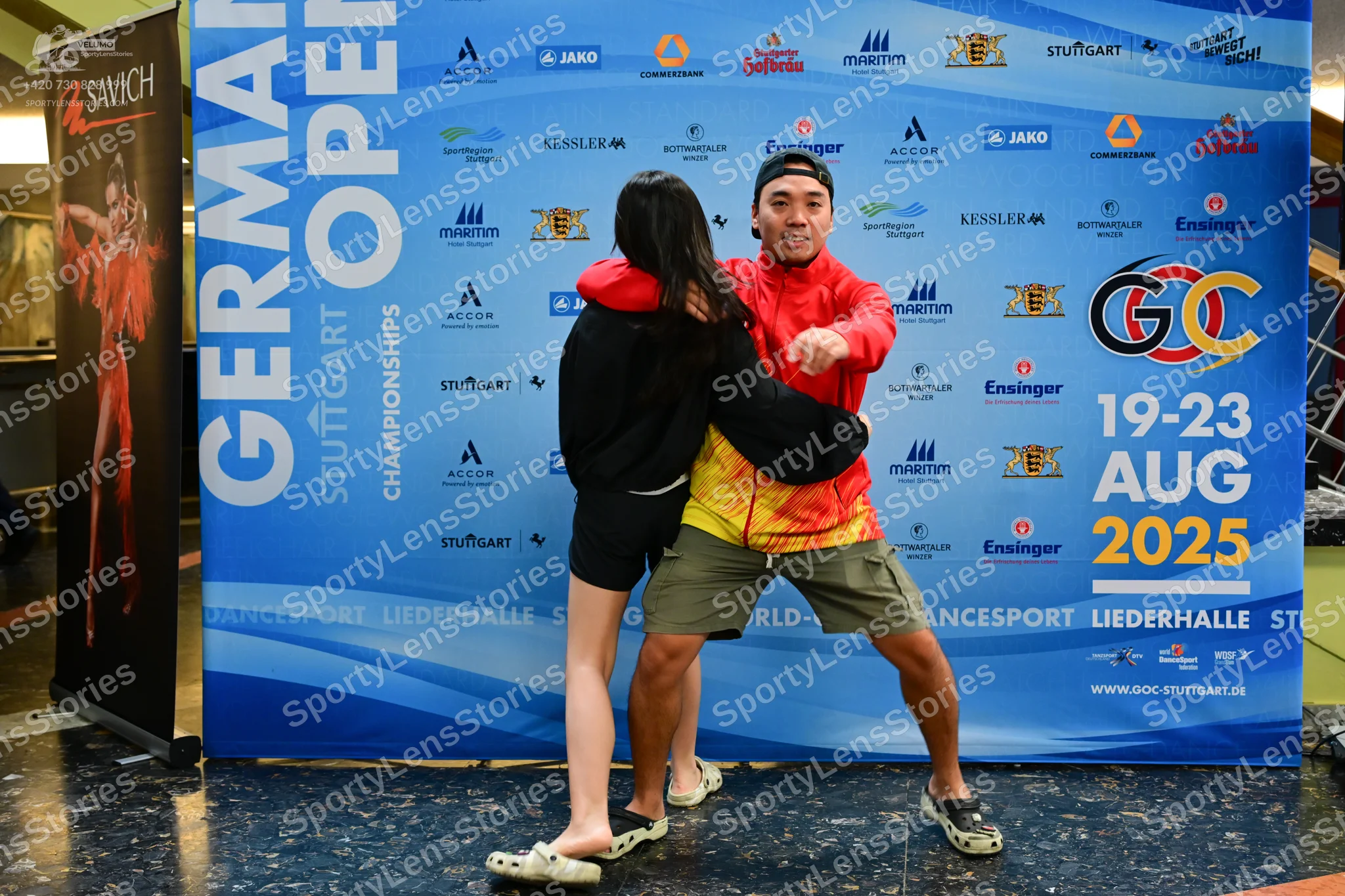 Dancesport competitor: Male dancer: red and yellow patterned jacket, olive green shorts, black cap, and