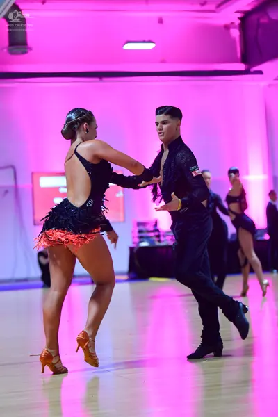 Dancesport competitor: Female dancer in foreground: black latin dress with red fringe at the hem