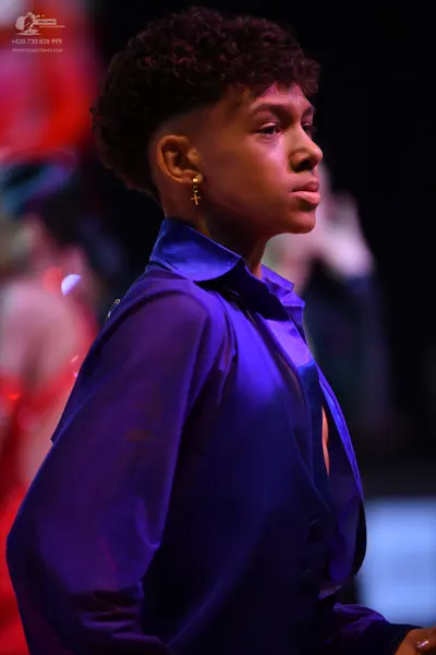 Dancesport competitor: Primary dancer: bright blue satin-like long-sleeved shirt and a gold cross earri