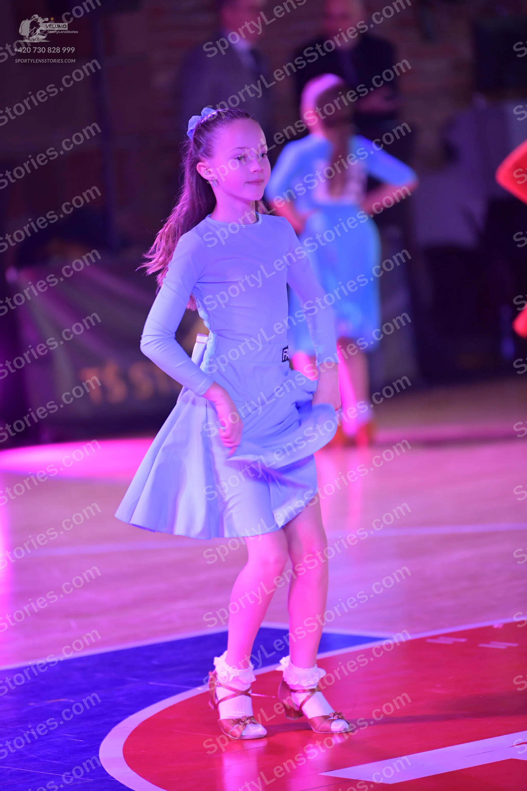 Dancesport competitor: Female dancer in foreground: light blue long-sleeve dress with a flared skirt, a