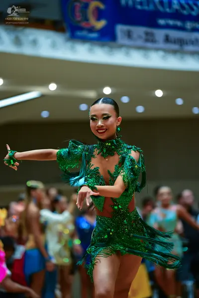 Dancesport competitor: Female dancer in foreground: green latin dance dress with green sequins, green f