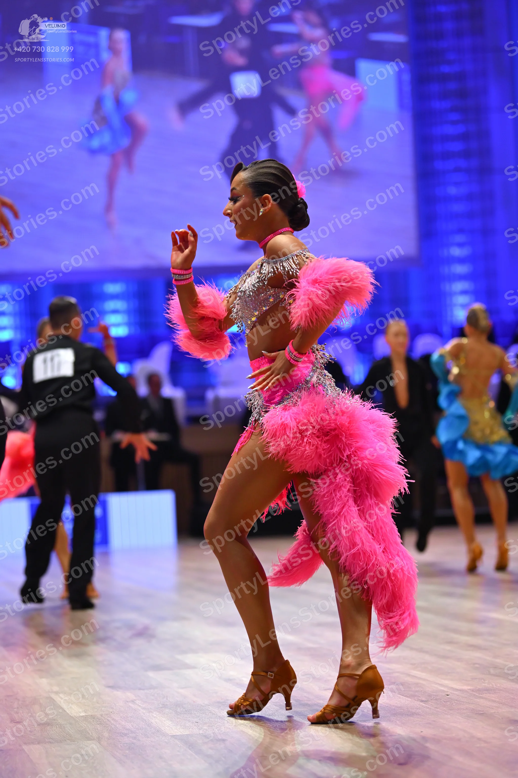 Dancesport competitor: Female dancer: pink Latin dress with a silver sequined bodice and large pink fea