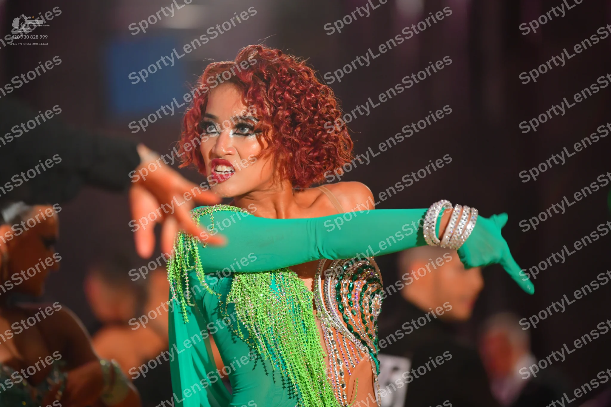 Dancesport competitor: Female dancer: green Latin dance dress with long sleeves, green fringe, and silv