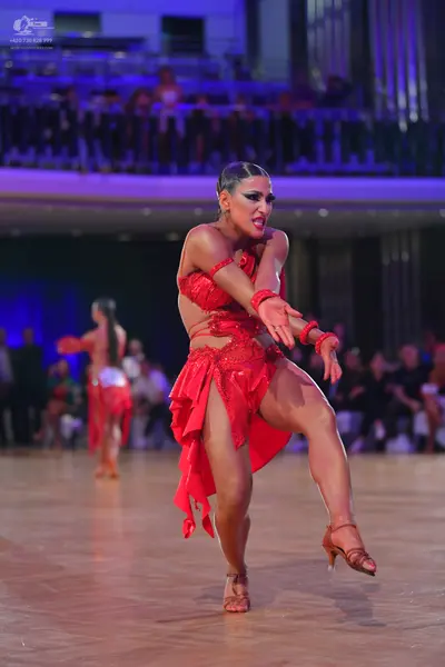 Dancesport competitor: Female dancer in foreground: red latin dress with sequins and cutouts