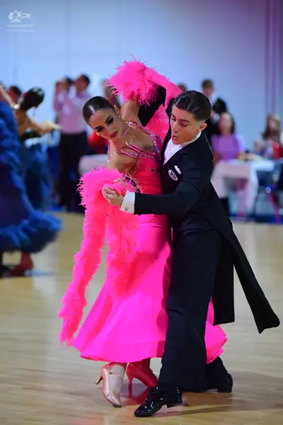 Dancesport competitor: Female dancer: bright pink ballroom gown with large pink feather accents on the 