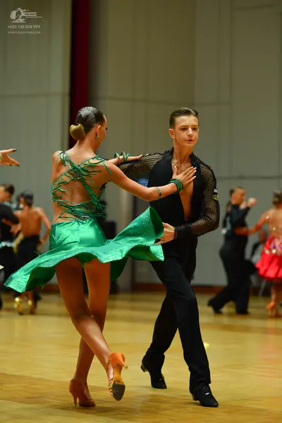 Dancesport competitor: Main female dancer: green latin dress with decorative green straps on the back a