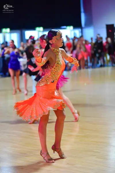 Dancesport competitor: Female dancer 1: orange Latin dress with gold sequin embellishments and a flared