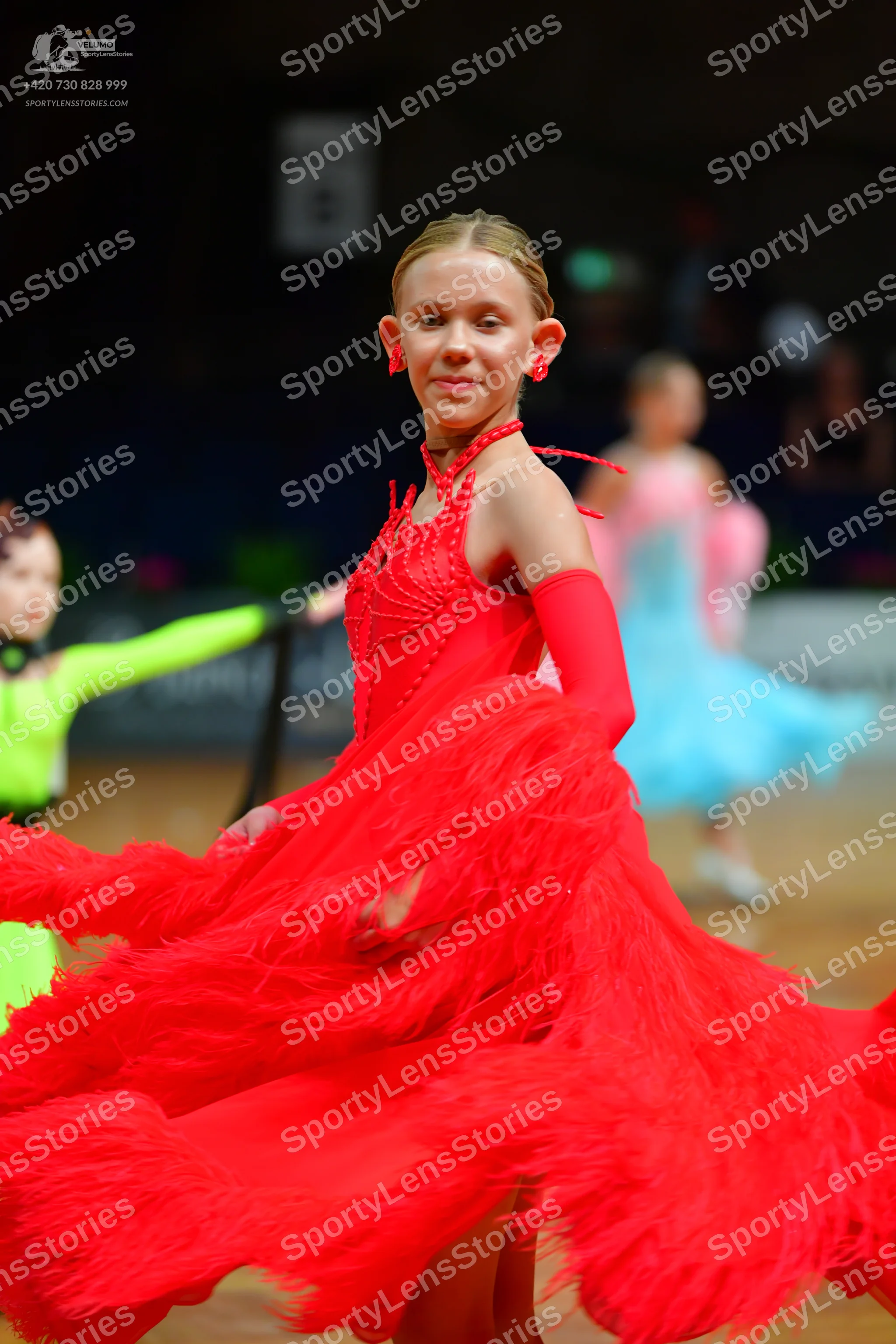 Dancesport competitor: Female dancer in foreground: red latin dress with extensive red fringe and a dec