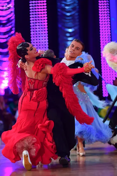 Dancesport competitor: Female dancer: red Latin dress with a corset-style bodice, ruffles, and long red