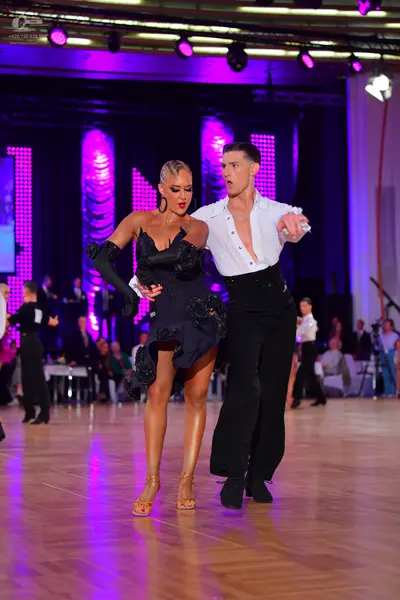 Dancesport competitor: Female dancer: black latin dress with 3D floral/rosette embellishments and long 