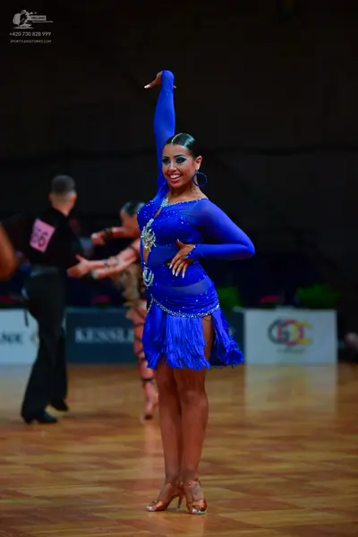Dancesport competitor: Female dancer: bright blue Latin dress with long sleeves, fringe, and sequins