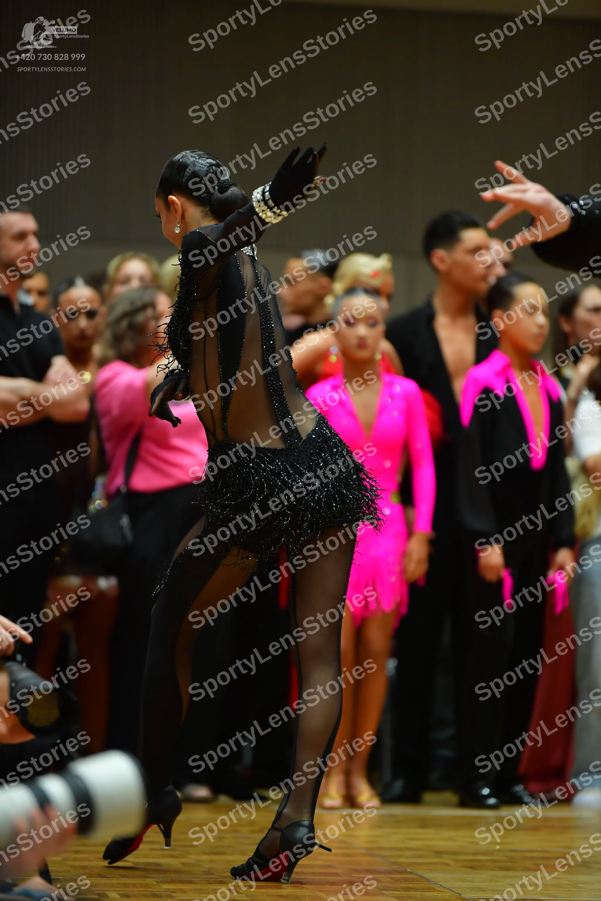 Dancesport competitor: Foreground female dancer: black long-sleeved sheer bodysuit with a sequined/frin