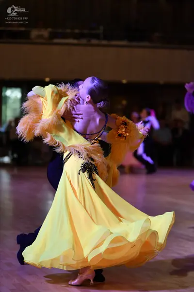 Dancesport competitor: Female dancer: yellow ballroom gown with feather trim on the sleeves and back, a