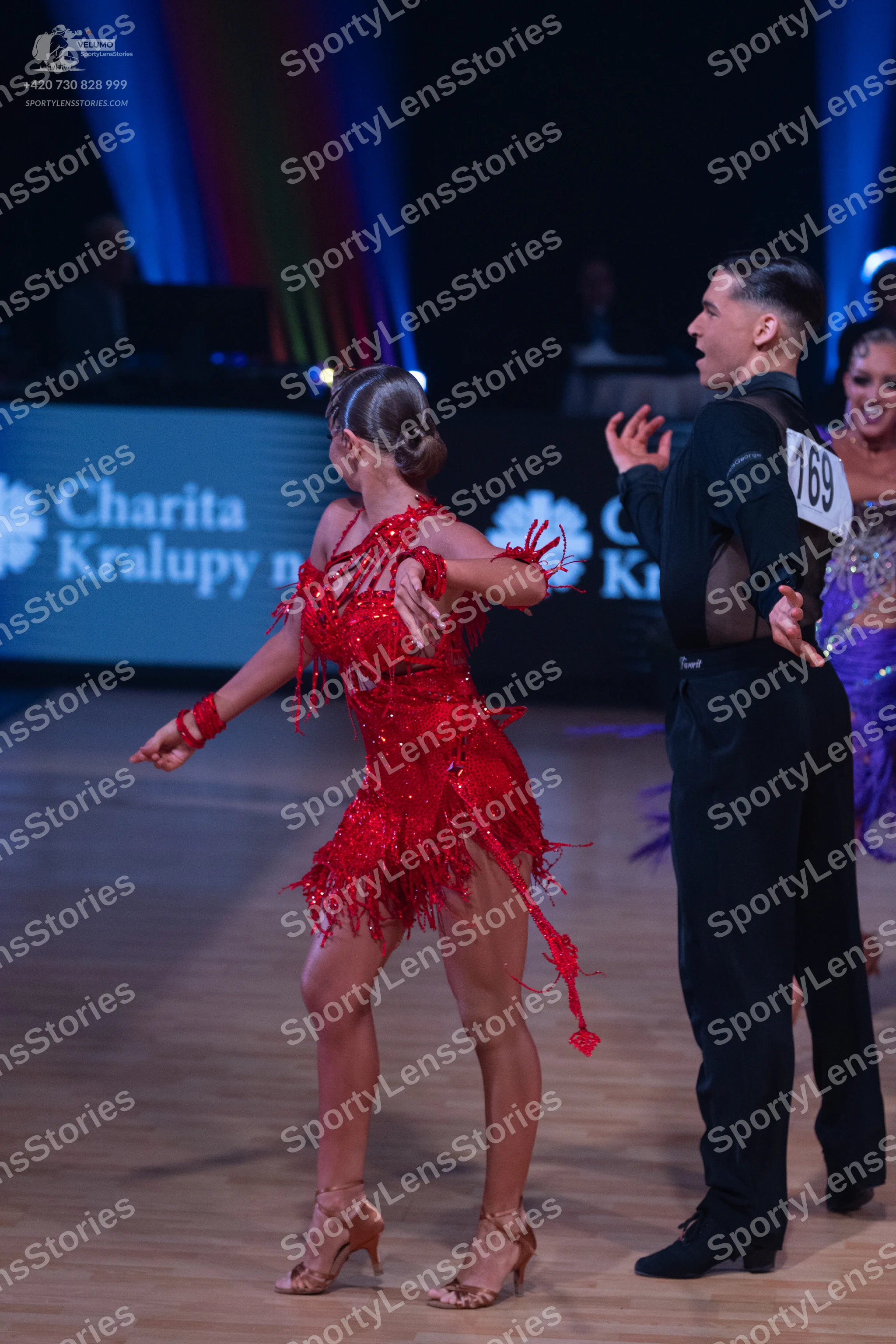 Dancesport competitor: Female dancer in foreground: red latin dress with fringe and matching red wristb
