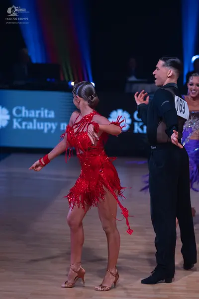 Dancesport competitor: Female dancer in foreground: red latin dress with fringe and matching red wristb