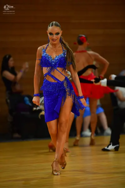 Dancesport competitor: Female dancer in foreground: royal blue sequined Latin dance costume with a halt