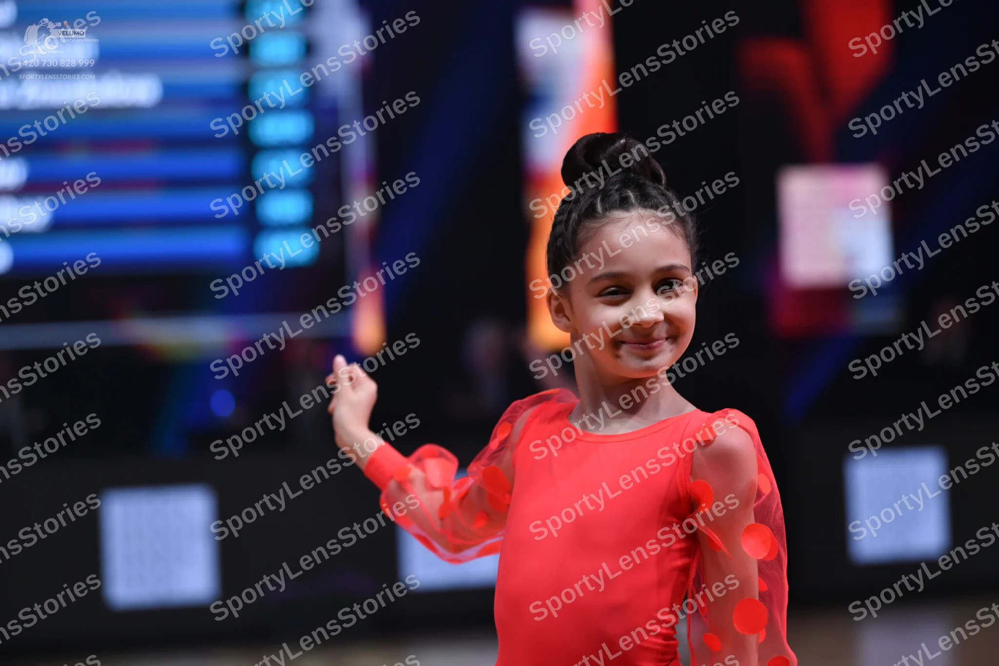 Dancesport competitor: Female dancer: red long-sleeved dress with sheer sleeves featuring red petal-lik