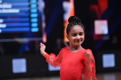 Dancesport competitor: Female dancer: red long-sleeved dress with sheer sleeves featuring red petal-lik