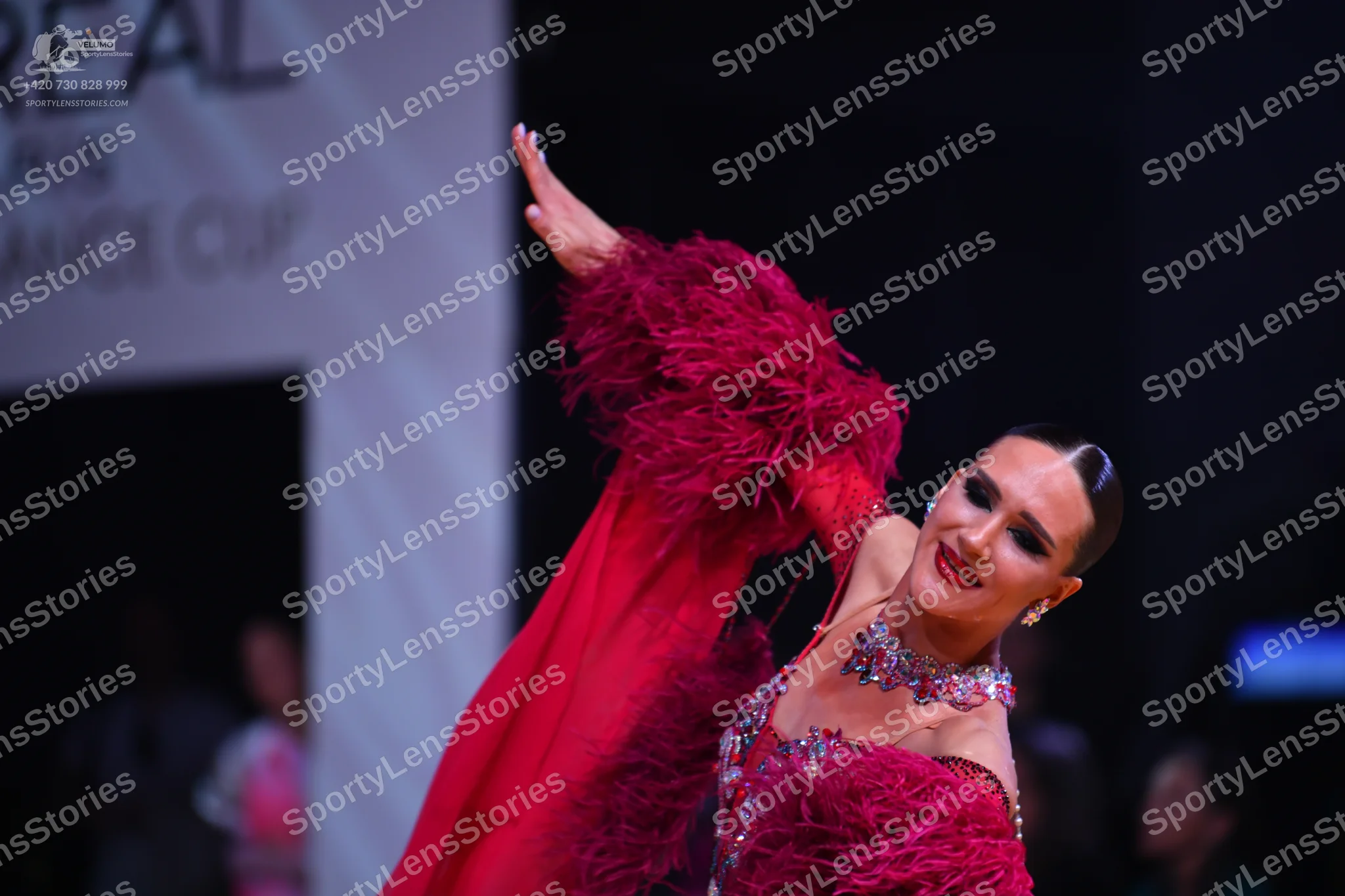 Dancesport competitor: Female dancer: deep red Latin dance dress with voluminous feathery sleeves and r