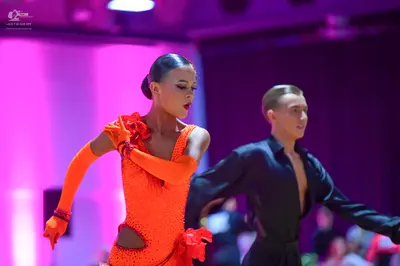Dancesport competitor: Female dancer: bright orange sequined Latin dress with a long sleeve/glove and a