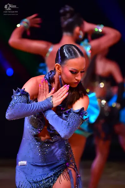 Dancesport competitor: Female dancer in foreground: periwinkle blue Latin dress with long ruffled sleev