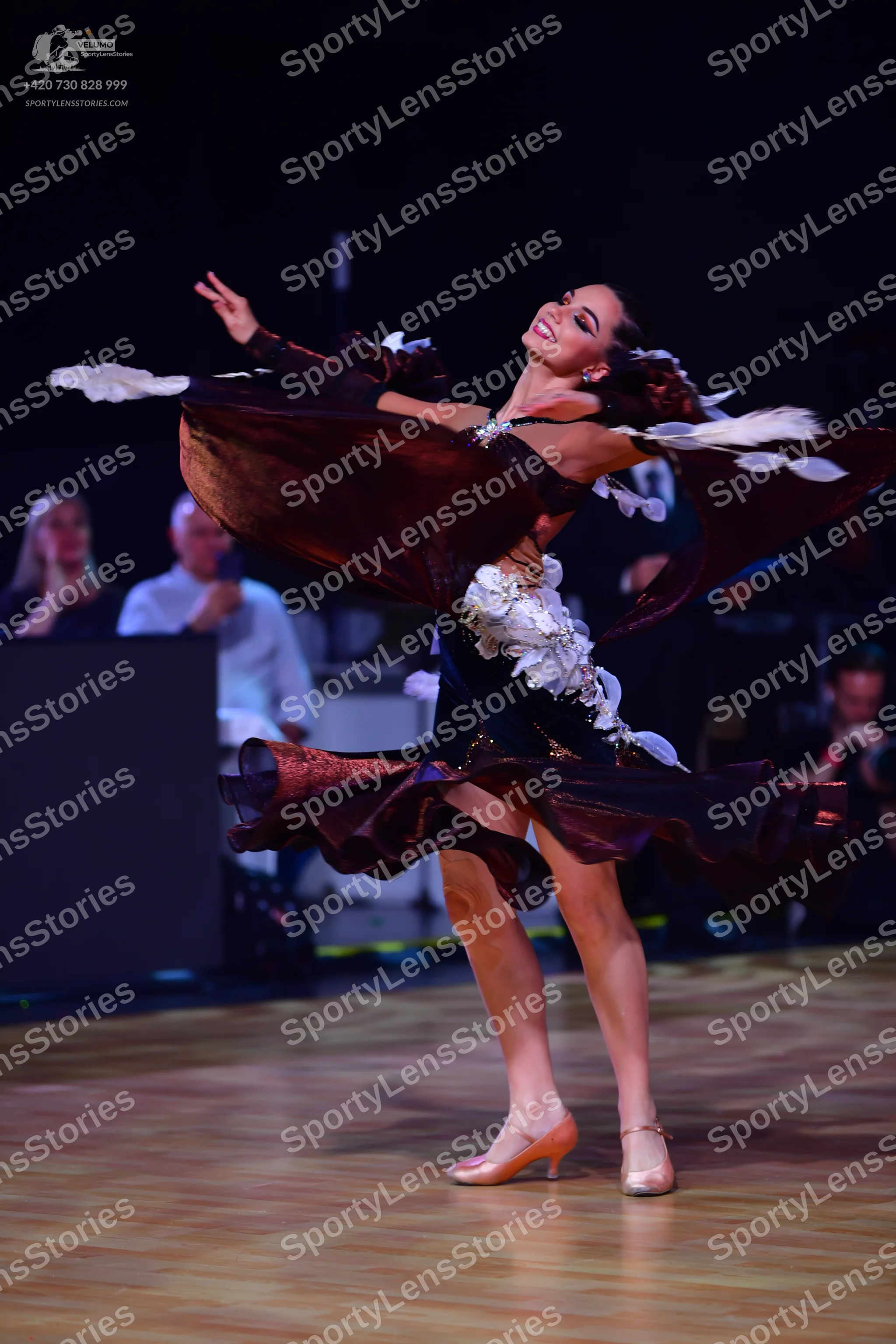 Dancesport competitor: Female dancer: a dark-colored Latin dance dress featuring large, voluminous, cop