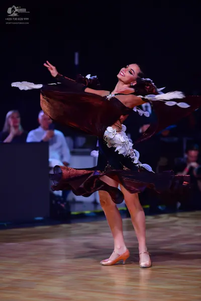 Dancesport competitor: Female dancer: a dark-colored Latin dance dress featuring large, voluminous, cop