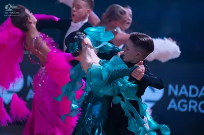 Dancesport competitor: Female dancer in foreground: teal latin dress with large, voluminous ruffled fab