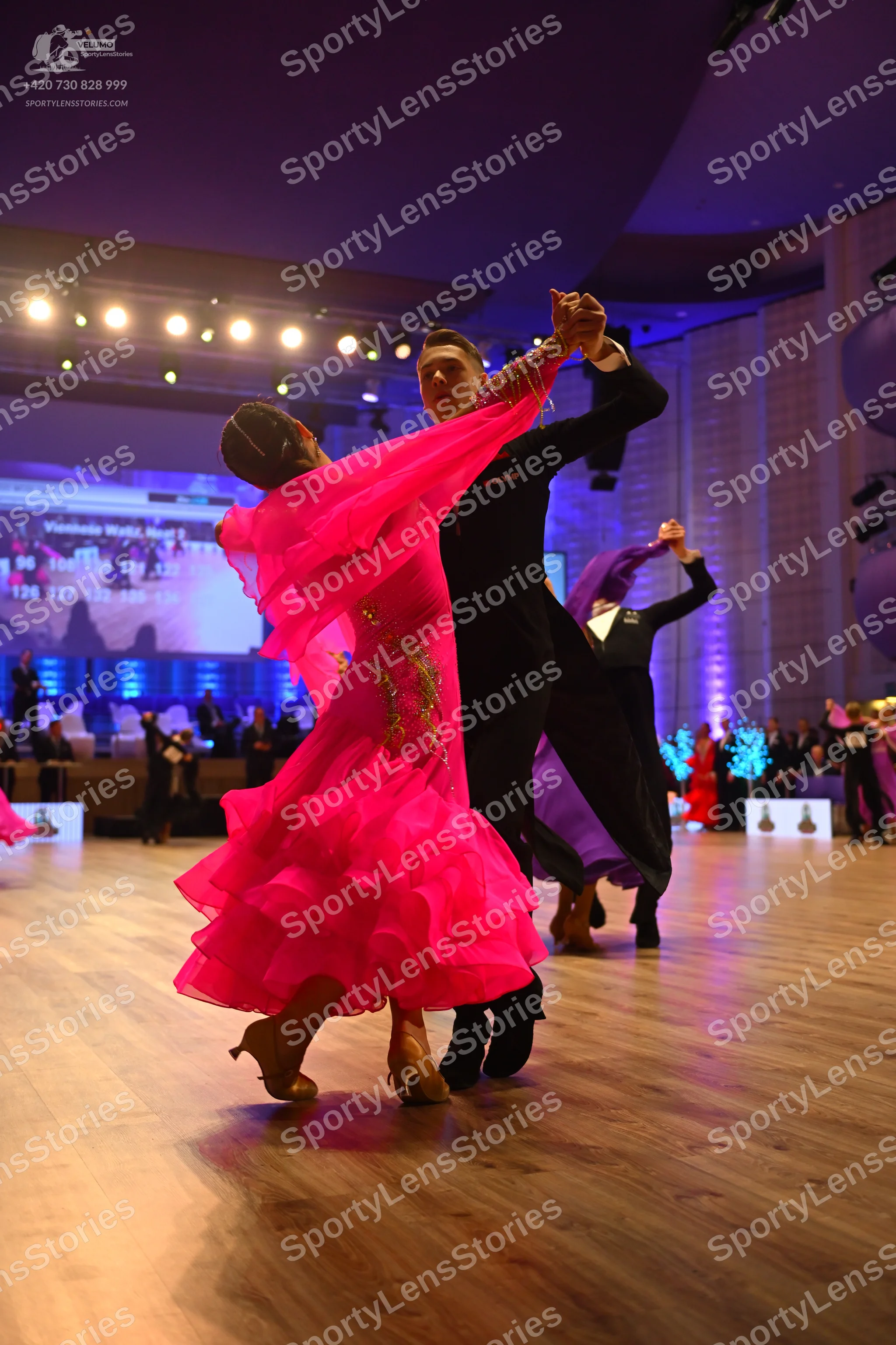 Dancesport competitor: Female dancer in foreground: bright pink ballroom dress with a voluminous ruffle