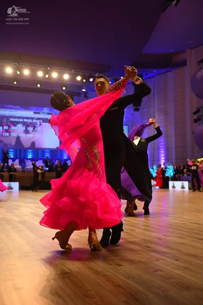Dancesport competitor: Female dancer in foreground: bright pink ballroom dress with a voluminous ruffle