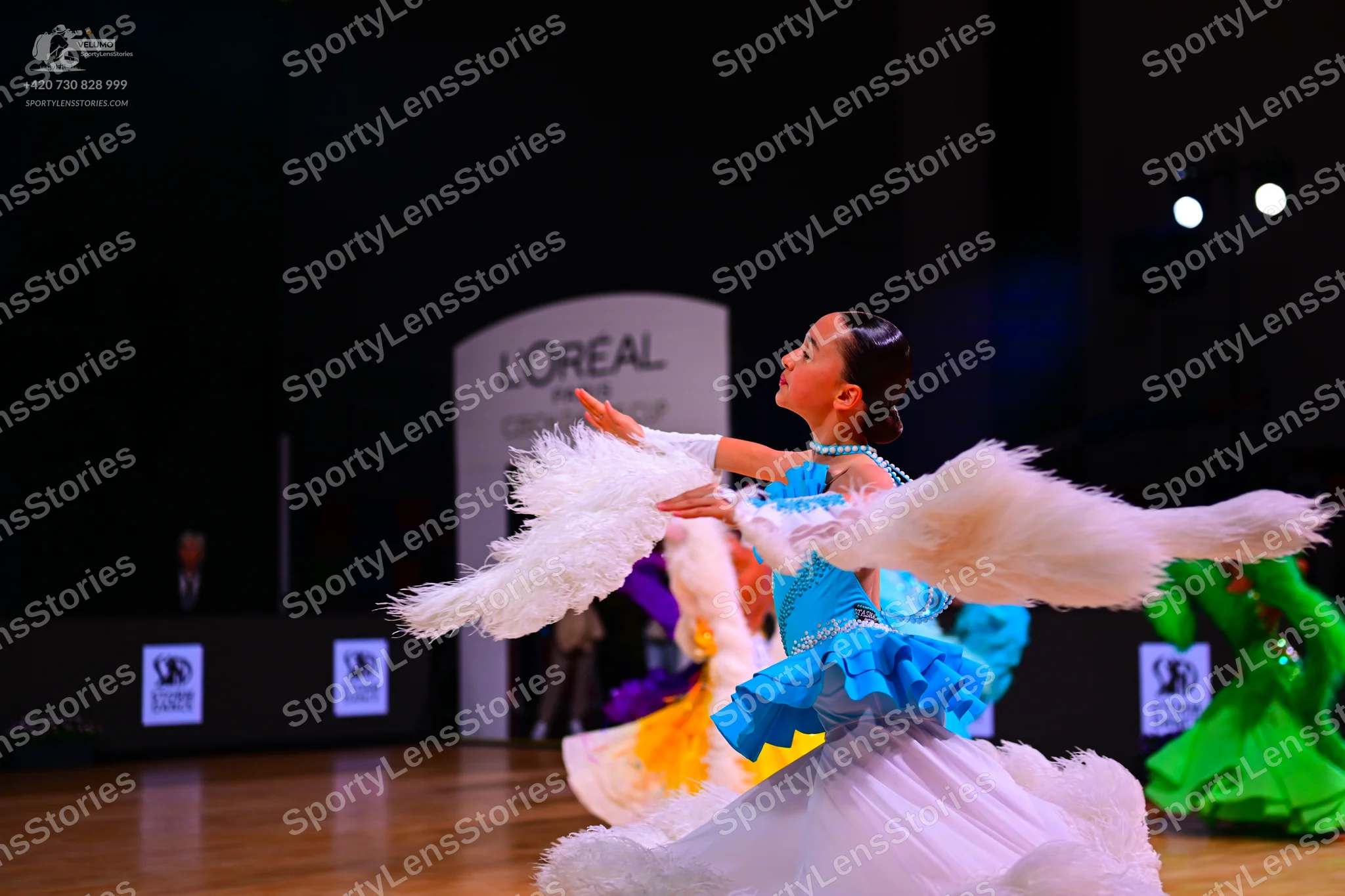 Dancesport competitor: Main female dancer: blue and white ballroom dress with large, white, fluffy arm