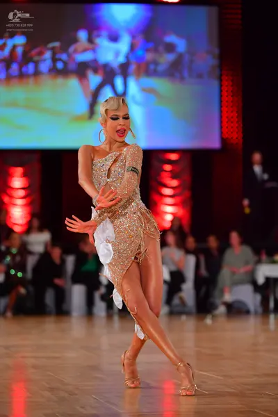 Dancesport competitor: Female dancer: gold sequined Latin dress with white fabric accents and large gol