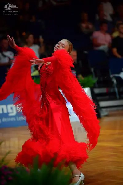 Dancesport competitor: Female dancer: red latin dress with large feather-like fringe on the sleeves and