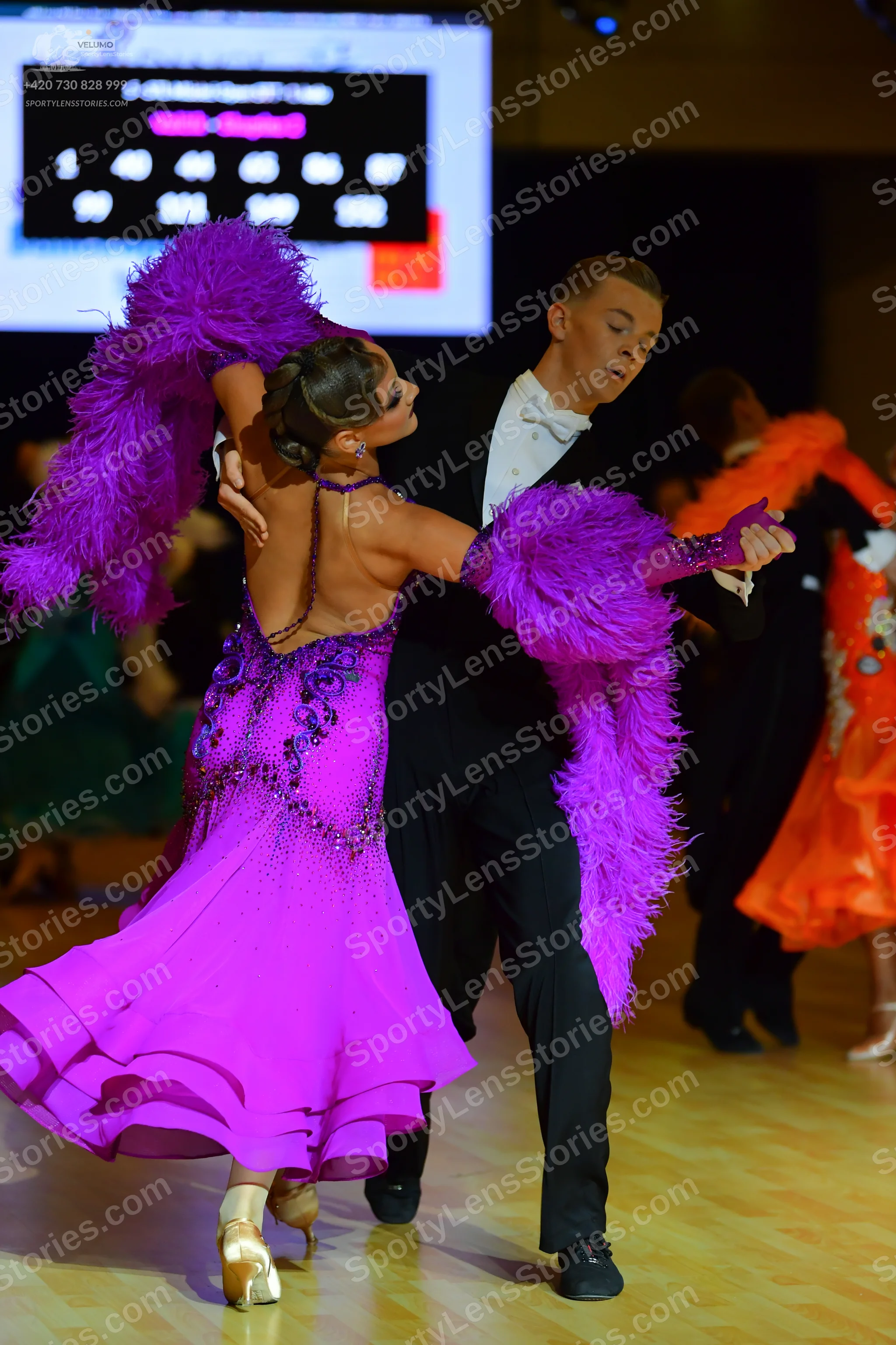 Dancesport competitor: Female dancer in foreground: magenta/purple dress with a sequined bodice and lar