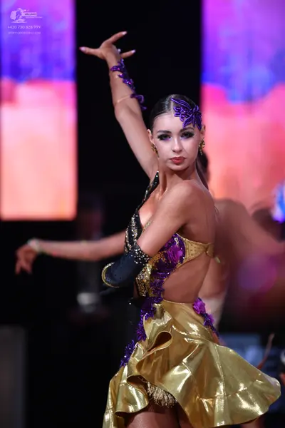 Dancesport competitor: Female dancer: gold, purple, and black latin dance costume with a metallic gold 
