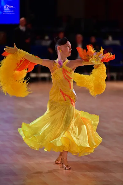 Dancesport competitor: Female dancer: yellow latin dress with orange accents and large yellow and orang