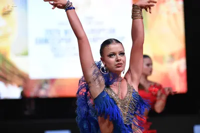Dancesport competitor: Female dancer in foreground: blue latin dress with long fringe and gold/silver s
