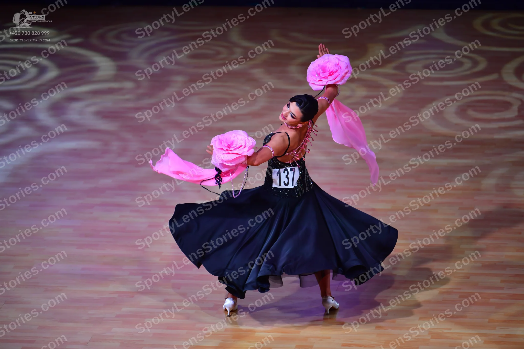 Dancesport competitor: Female dancer: black ballgown with large, flowing pink fabric accessories on the