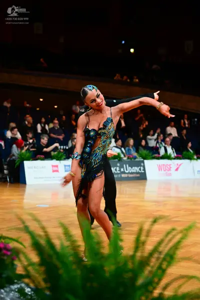 Dancesport competitor: Female dancer: dark Latin dress with intricate blue, gold, and multi-colored seq