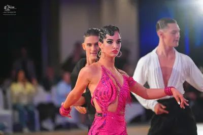 Dancesport competitor: Female dancer: pink Latin dress with sequins and fringe, featuring cutouts, pair