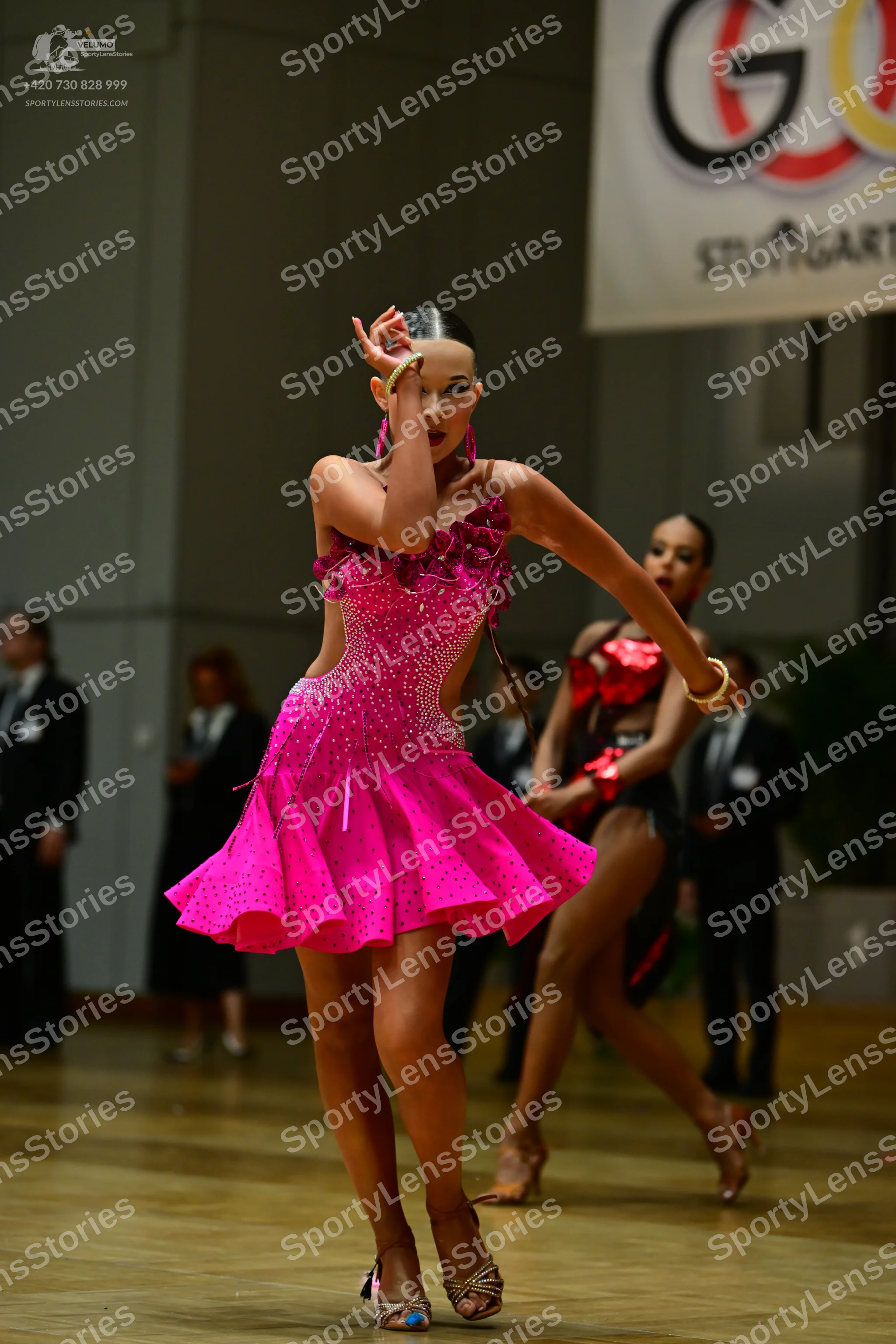 Dancesport competitor: Female dancer in foreground: bright pink Latin dance dress with sequins, featuri