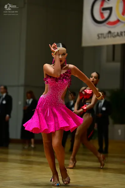 Dancesport competitor: Female dancer in foreground: bright pink Latin dance dress with sequins, featuri