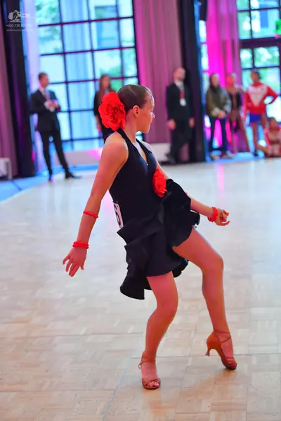 Dancesport competitor: Female dancer: black sleeveless Latin dress with a ruffled skirt, a large red fl
