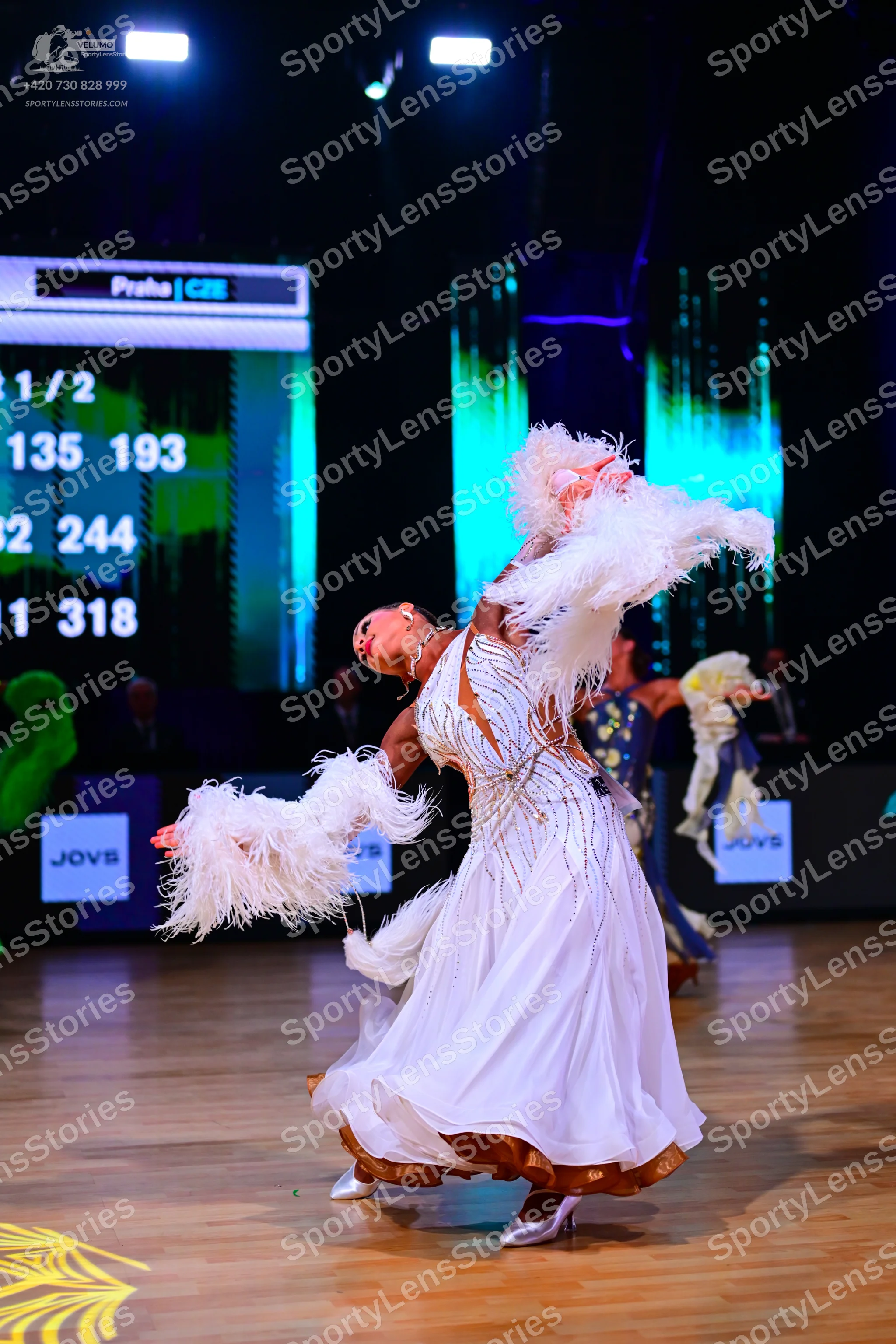 Dancesport competitor: Female dancer in foreground: white ballroom gown with gold/bronze sequin and emb