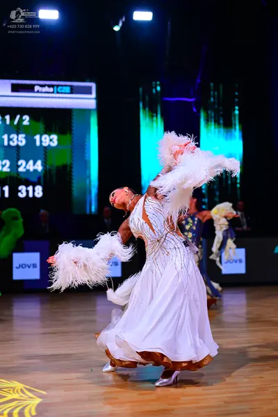 Dancesport competitor: Female dancer in foreground: white ballroom gown with gold/bronze sequin and emb