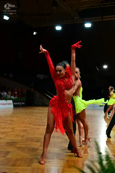 Dancesport competitor: Female dancer in foreground: red Latin dress with long sleeves and fringe