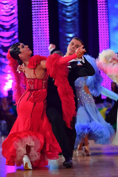 Dancesport competitor: Female dancer in foreground: red latin/ballroom dress with lace bodice and large